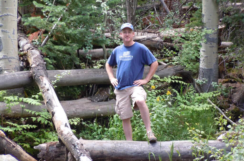 A man standing with his foot on a log in the woods representing accomplishment..